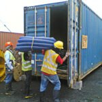 Workers carrying coiled industrial conduit during container loading operations