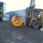Forklift transporting a large industrial cable reel near shipping containers