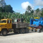 Yellow tractor head hauling heavy industrial equipment through a rural area