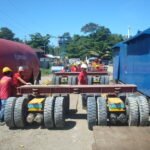 Transport crew assembling modular multi-axle trailer units beside industrial cargo