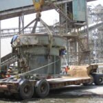Crane positioning heavy industrial equipment onto a low-bed trailer