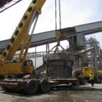Crane crew conducting a heavy equipment lifting and loading operation at an industrial facility