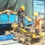 Workers operating a hydraulic jacking system beneath oversized industrial equipment