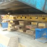 Close-up of hydraulic jacks, timber cribbing, and steel supports beneath heavy equipment