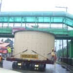 Oversized cylindrical equipment passing beneath a pedestrian overpass on a modular trailer