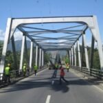 Oversized cargo convoy crossing a steel bridge with transport personnel managing traffic