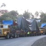 Two tractor heads hauling covered oversized equipment on a modular multi-axle trailer