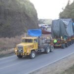 Heavy transport convoy carrying covered oversized equipment along a mountain road