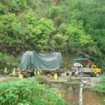 Heavy transport convoy carrying covered industrial equipment on a narrow mountain road
