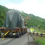Rear view of covered oversized cargo on a modular trailer along a rural road