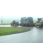 Heavy transport convoy navigating a wet curved road with covered oversized cargo