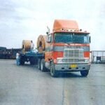Front view of a tractor head hauling steel sheet rolls on a low-bed trailer
