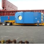 Large blue industrial module transported on a low-bed trailer at a port facility