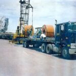 Blue tractor head transporting steel sheet rolls on a low-bed trailer